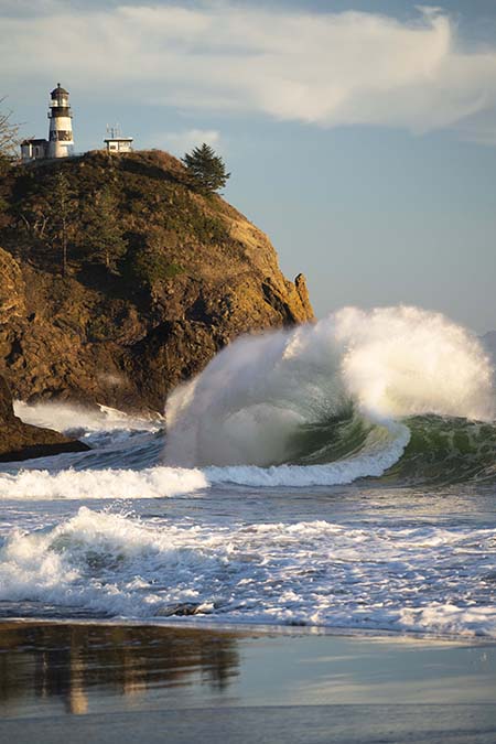 Image of a wave with a lighthouse in the distance taken by Dan Merkel.