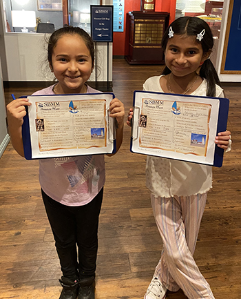 Two girls holding up artwork in the museum.